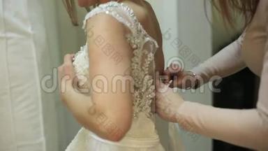 漂亮的女孩在婚纱店里试穿婚纱，店员正在试衣间帮新娘